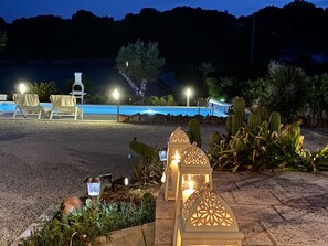 Un espace extérieur aménagé pour la nuit, avec une piscine, des chaises longues et des lanternes décoratives.