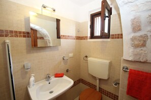 Une salle de bain équipée d’un lavabo, d’un miroir, de toilettes et d’une fenêtre, avec une serviette accrochée au mur.