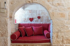 Pared de pedra com um banco acolchoado vermelho e duas decorações em formato de coração.