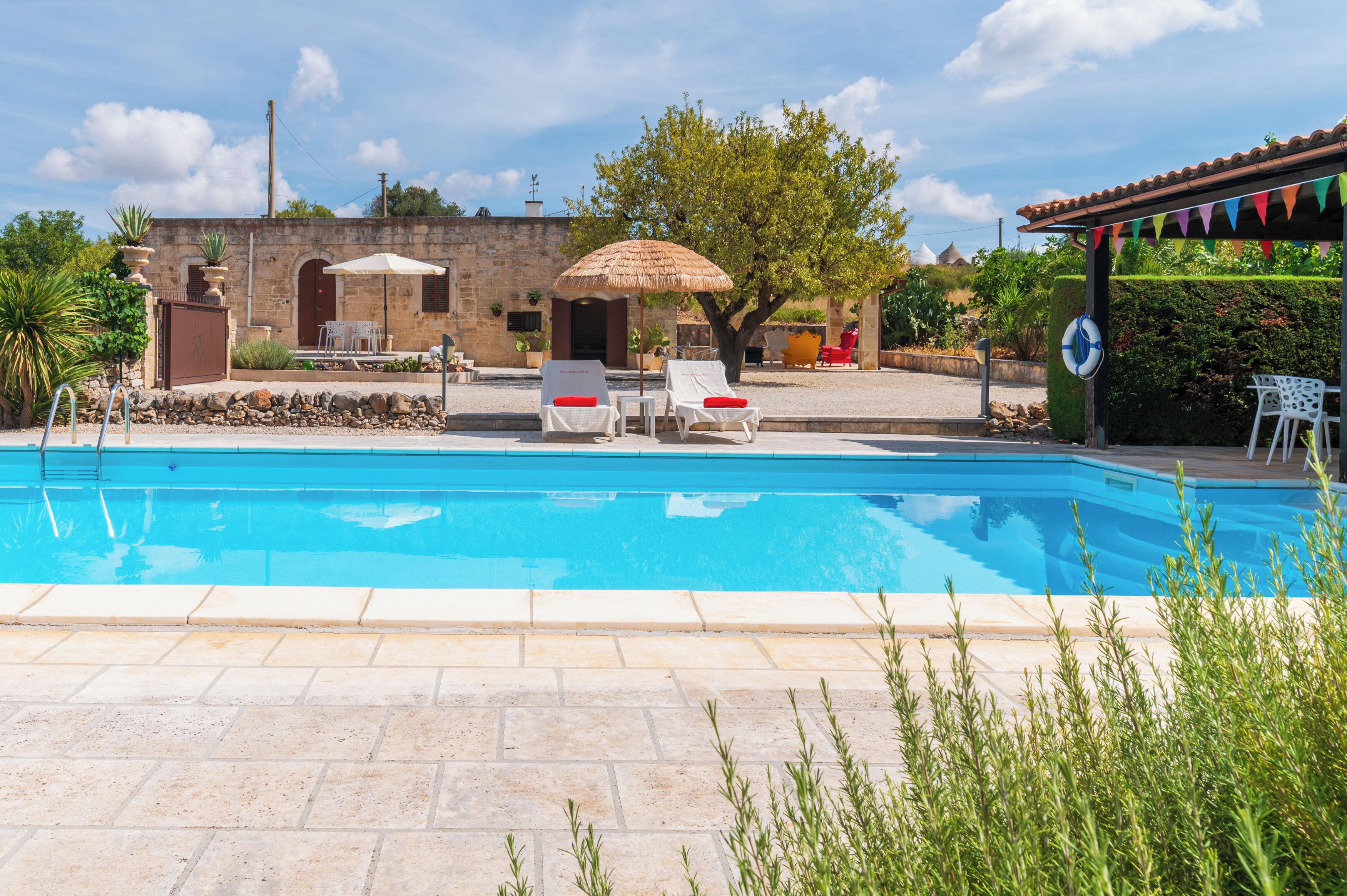 A swimming pool with lounge chairs and umbrellas, surrounded by stone walls and greenery.