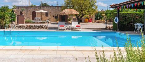 A swimming pool with lounge chairs and umbrellas, surrounded by stone walls and greenery.