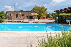 Una piscina con sillas de descanso y sombrillas, rodeada de muros de piedra y vegetación.