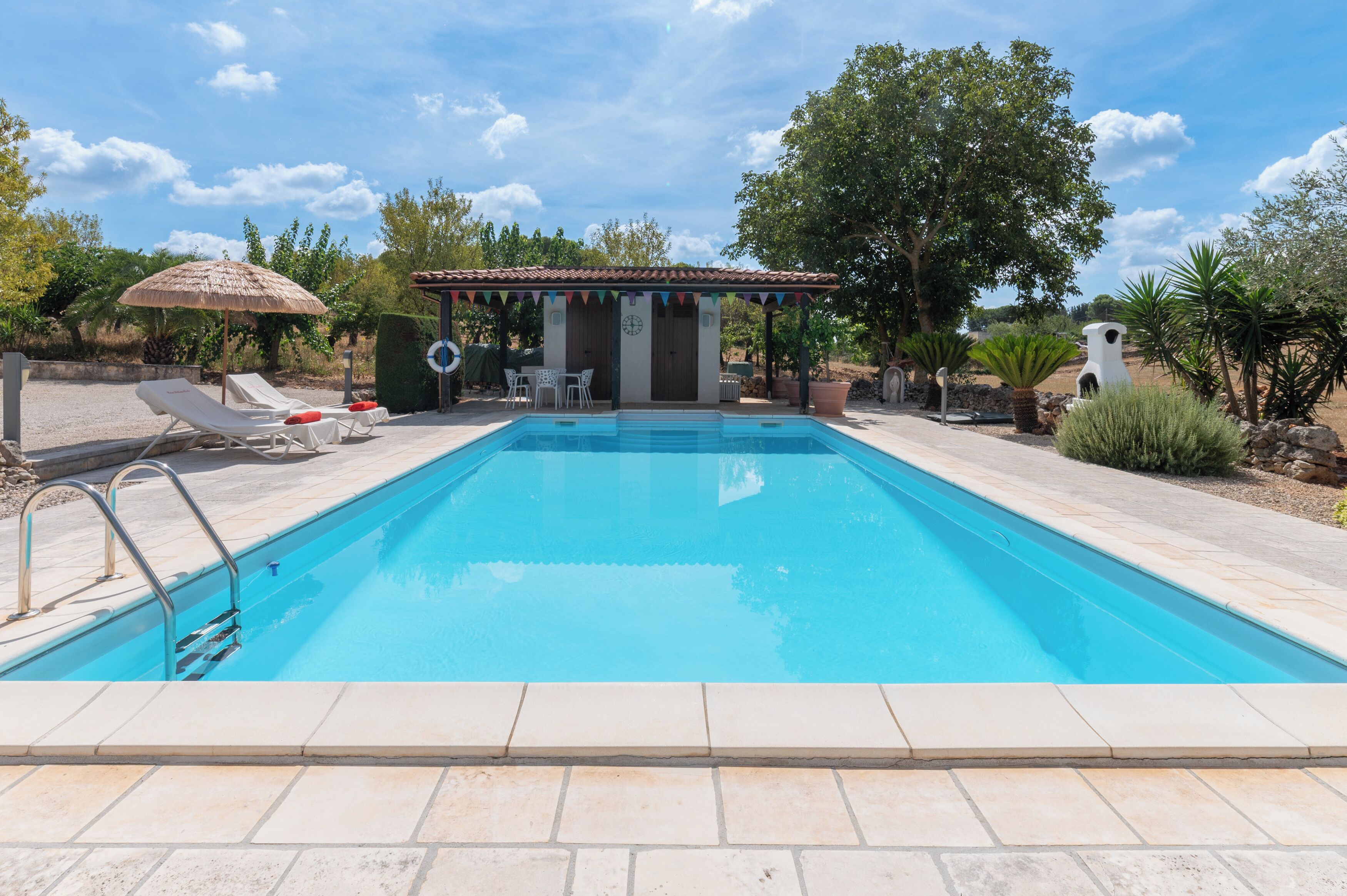 Ein Swimmingpool mit Liegestühlen und einer überdachten Sitzgelegenheit.