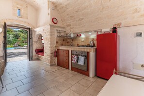 A kitchen with stone walls, a red refrigerator, and a view of a pool outside.
