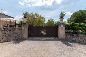 Una entrada protegida por un muro de piedra y una verja metálica con un símbolo de sol.