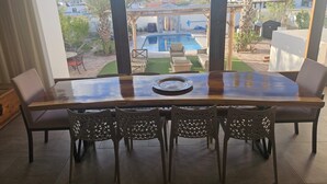 A dining area with a large wooden table and four chairs, overlooking a swimming pool and outdoor seating. - Casa Marimar with private heated pool at Laguna Shores Resort (Puerto peñasco)
