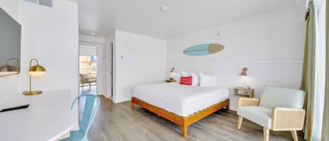 A modern hotel room with a wooden bed, a desk, a blue chair, and a wicker armchair.