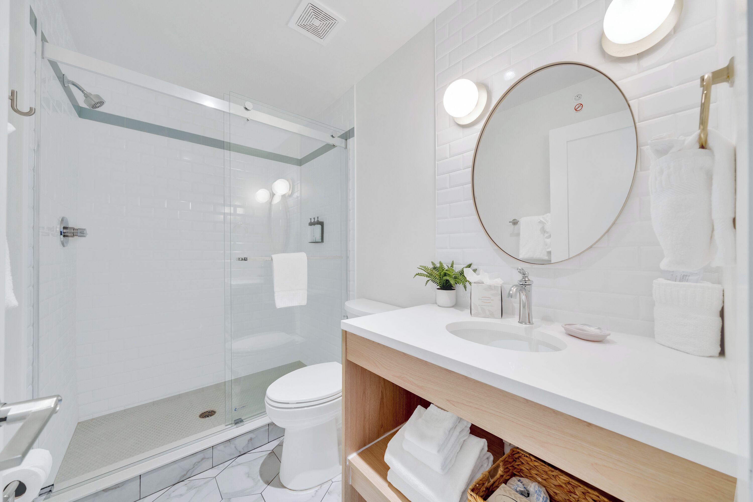 A modern bathroom with a glass-enclosed shower, a toilet, and a sink with a mirror above.