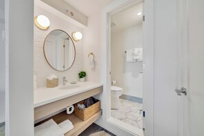 A modern bathroom with a white vanity, a round mirror with lights, a toilet, and a shower area. - Madison Resort Wildwood Crest (Wildwood Crest)