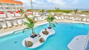 Un espace piscine avec des chaises longues et des parasols, un bâtiment avec un toit rouge et une vue sur la plage.