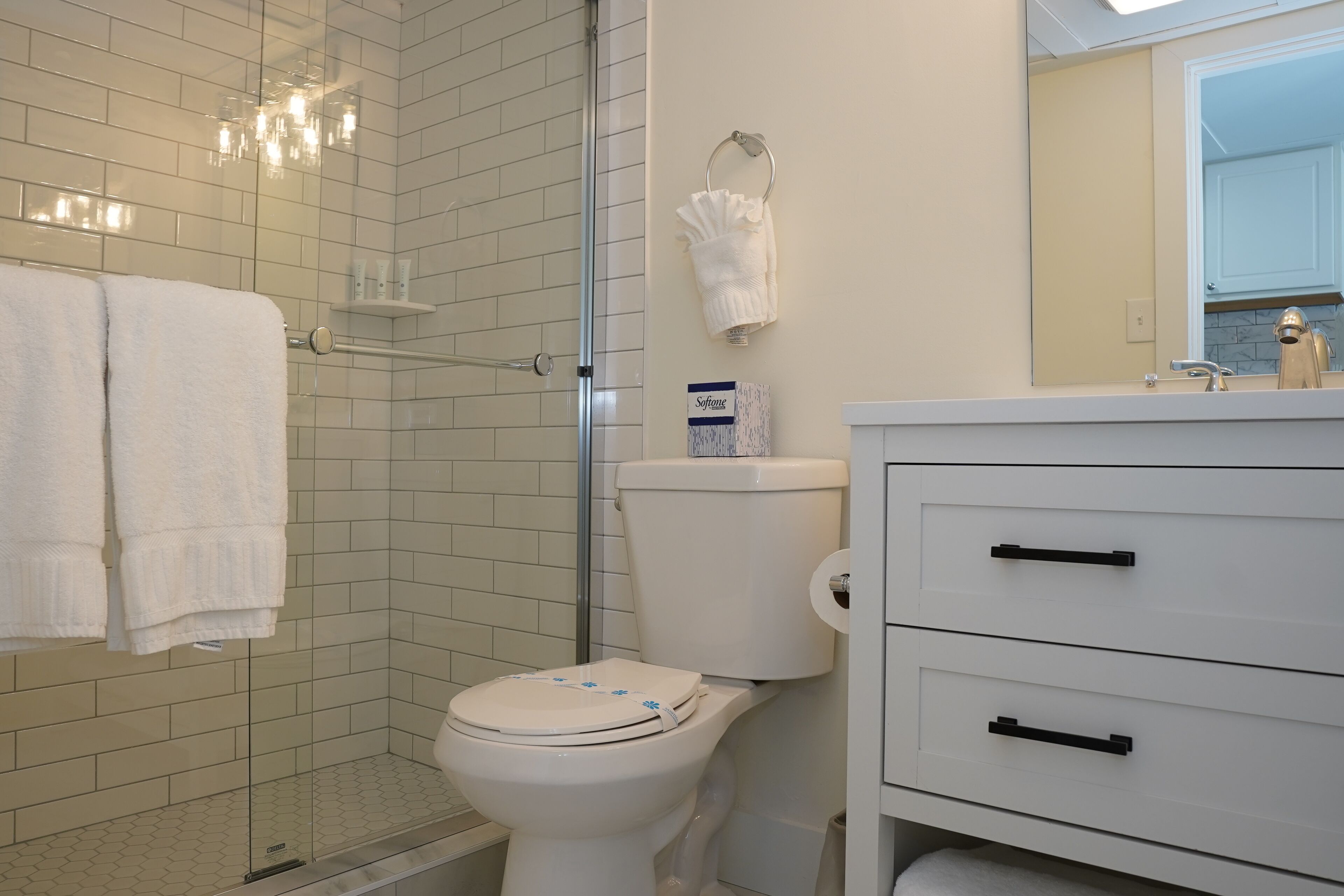 Un baño con inodoro, cabina de ducha de vidrio, tocador con espejo y perchero.