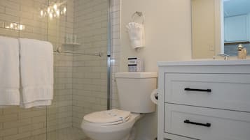 Une salle de bain comprenant des toilettes, une douche en verre, un meuble-lavabo avec un miroir et un porte-serviettes.