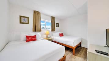 Habitación de hotel con dos camas, una mesita de noche con lámpara, televisión y ventana con cortinas.