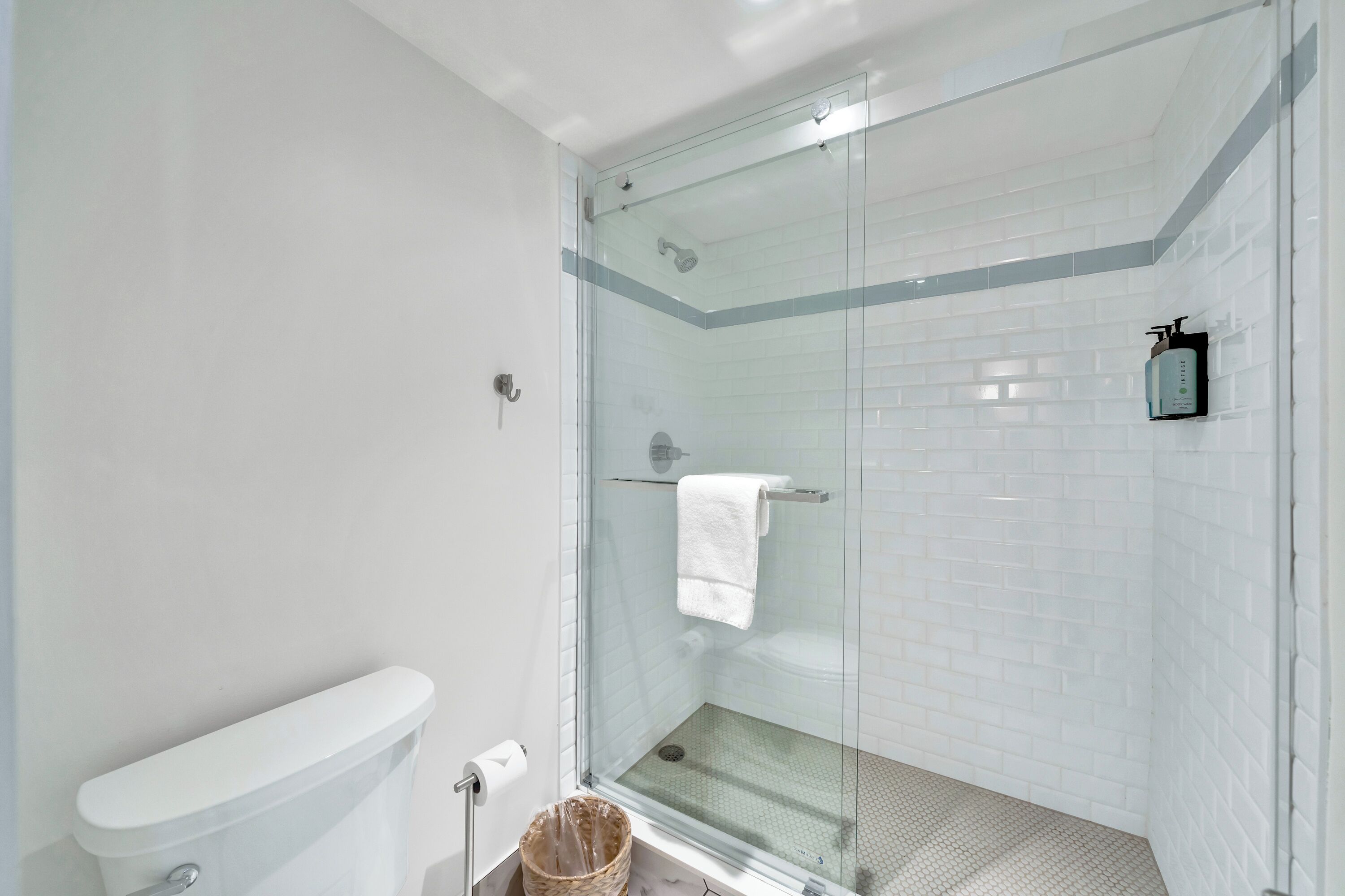 A modern bathroom with a glass-enclosed shower, white tiled walls, and a visible toilet.