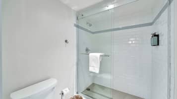 A modern bathroom with a glass-enclosed shower, white tiled walls, and a visible toilet.