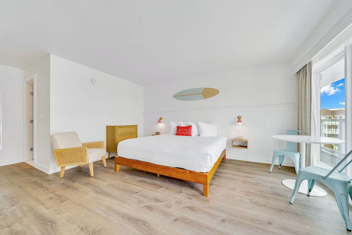 Ein modernes Hotelzimmer mit einem hölzernen Bett, weißen Wänden und einem großen Fenster mit Blick auf den Himmel.