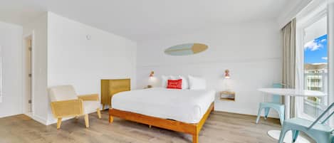 A modern hotel room with a wooden bed, white walls, and a large window offering a view of the sky.
