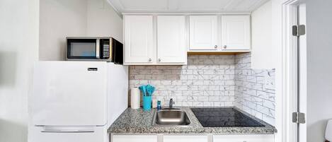 A compact kitchen with white cabinets, a microwave, a sink, and a fire exit sign.