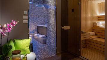 A modern bathroom with a glass shower enclosure, a wooden sauna, and a seating area with a green cushion.