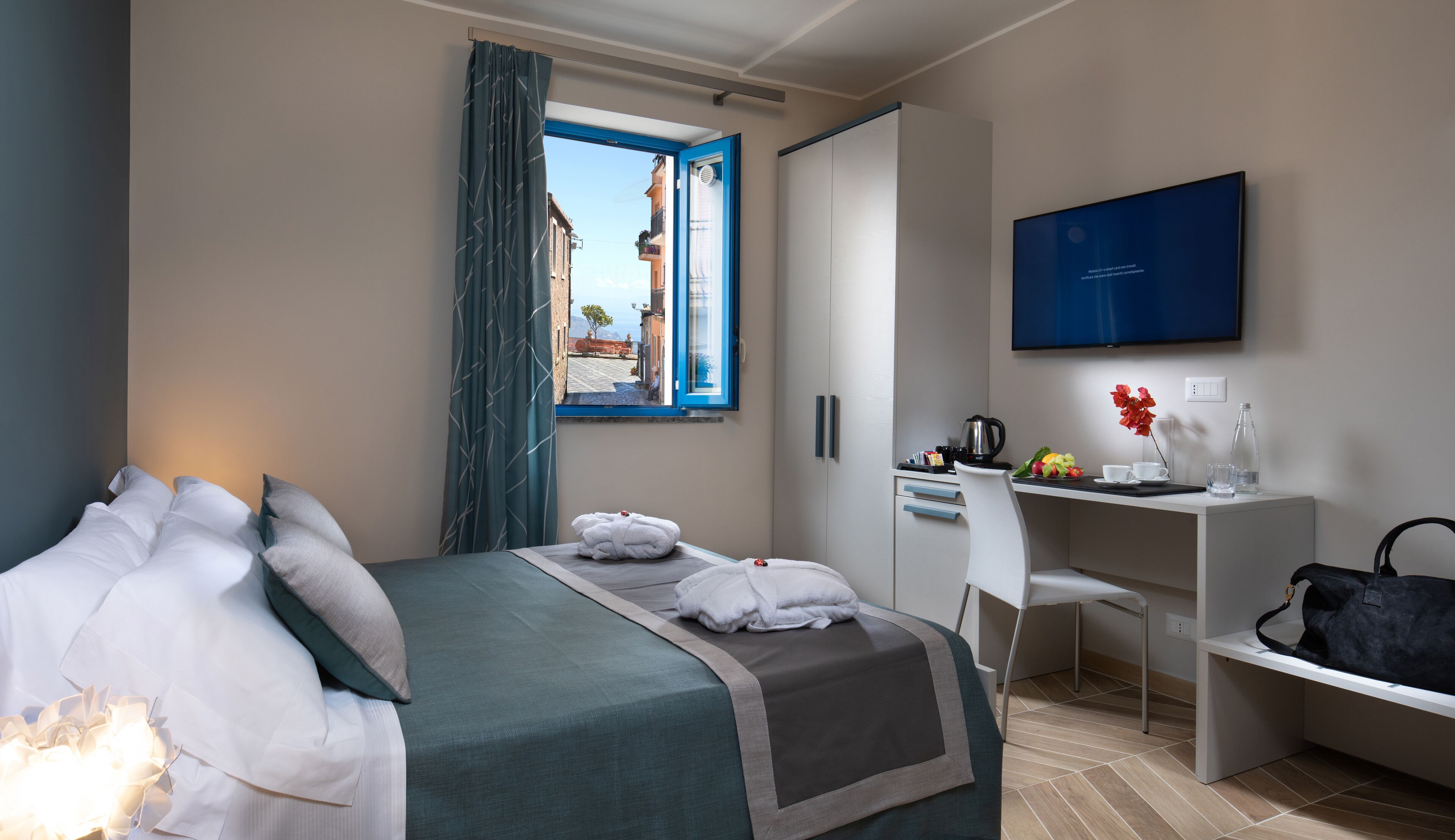 A hotel room with a bed, a desk, a chair, a TV, and a window with curtains.