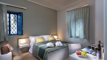 Habitación de hotel con una cama, mesitas de noche, un escritorio con una botella y vasos, y una ventana con cortinas.