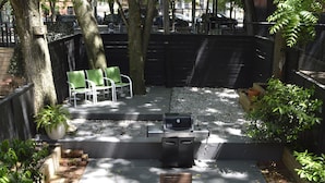 Ein Patio mit einem Holztisch und -stühlen, umgeben von Bäumen und einer Ziegelmauer.