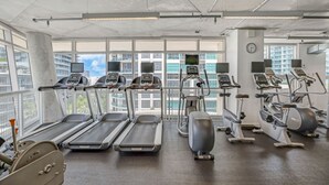 A gym with treadmills, elliptical machines, and stationary bikes, large windows with a city view, and a clock on the wall. - Midtown Miami 2-BD | Pool+Sauna | Gym | Mini Golf (Miami)