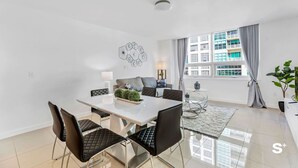 A modern dining area with a white table, black chairs, and a decorative wall piece. - Midtown Miami 2-BD | Pool+Sauna | Gym | Mini Golf (Miami)