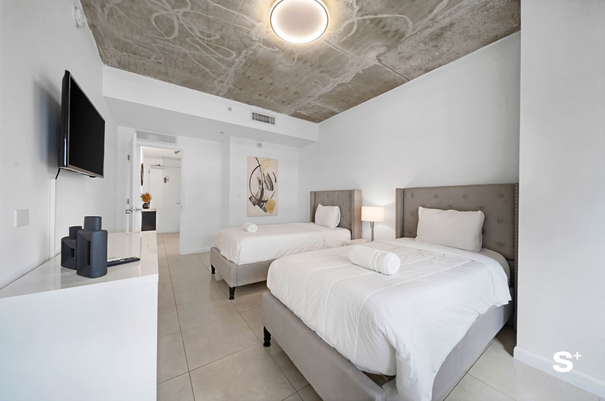 Een moderne hotelkamer met twee bedden, een flatscreen televisie, een bureau met lamp en een plafond met een ronde verlichtingsarmatuur.