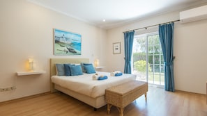 A bedroom with a bed, a wicker bench, a painting, a window with curtains, and an air conditioning unit. - Holiday home w/ heatable pool & BBQ (Almancil)