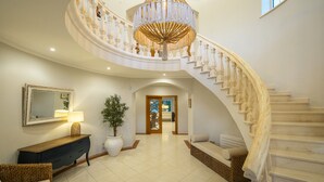 A grand staircase with a chandelier, a mirror, a potted plant, and a console table.