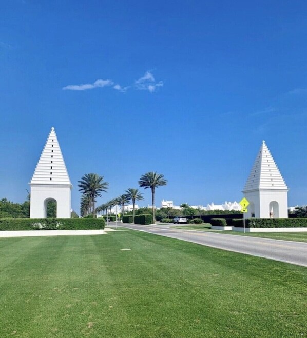 A white monument with a pointed top, surrounded by a well-maintained lawn and palm trees.