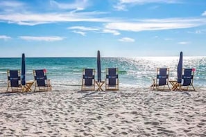 Una playa con cuatro sillas de playa y sombrillas dispuestas en fila.