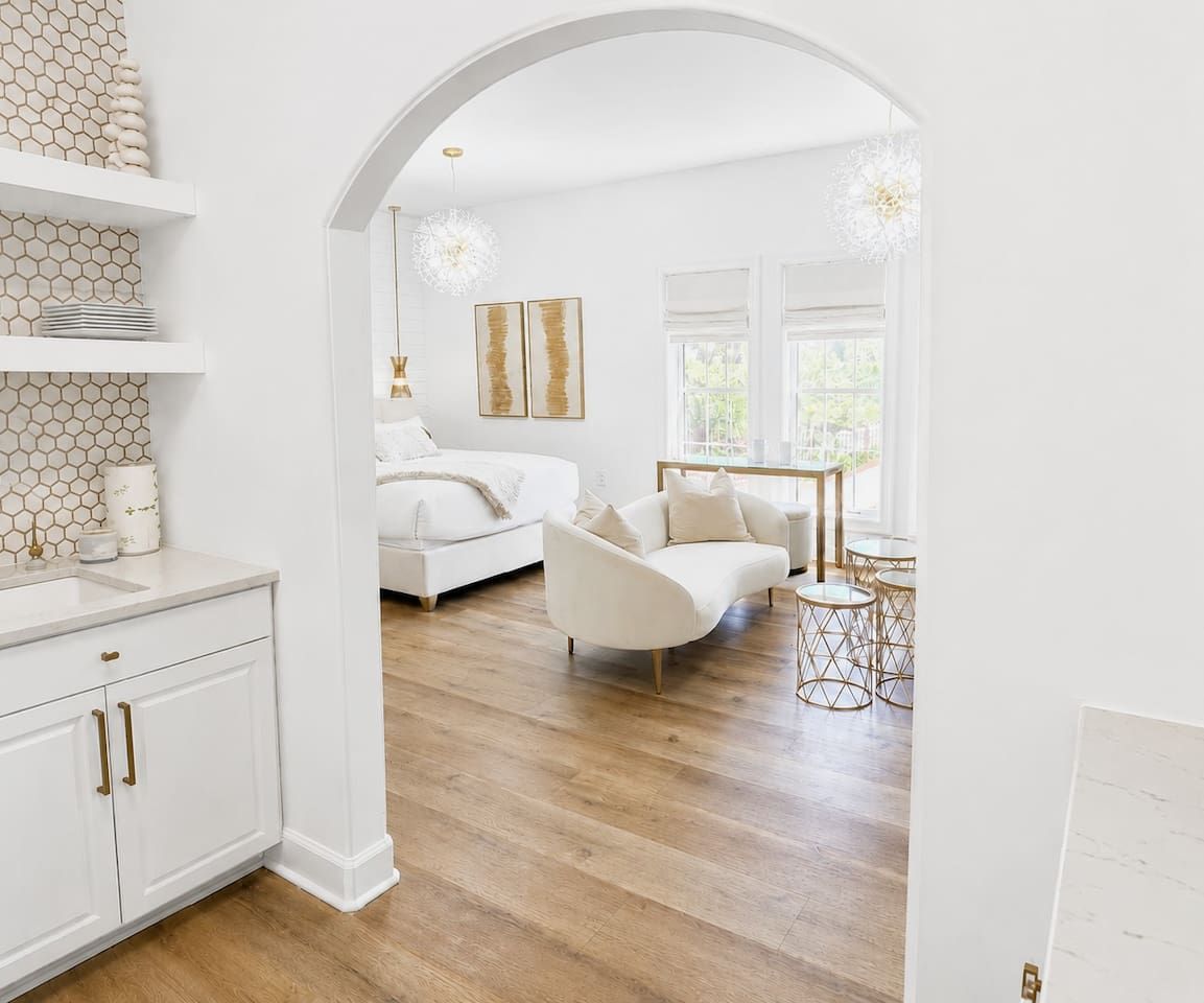 Een modern interieur met een witte bank, een eettafel met stoelen, en een keuken met witte kasten en een backsplash van hexagontegels.