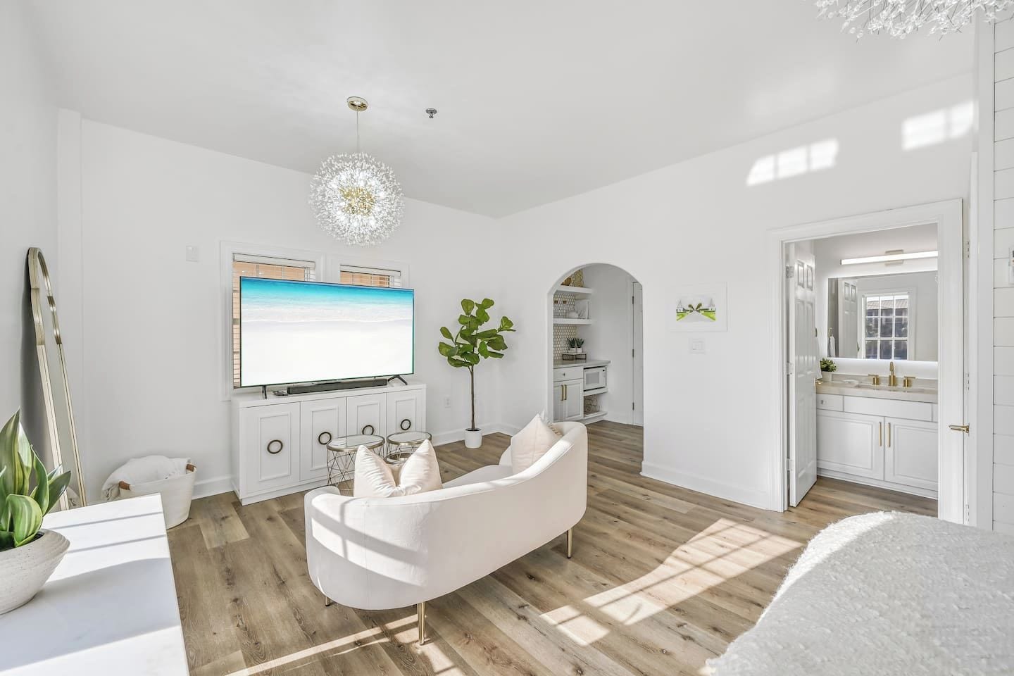 A modern living room with a flat-screen TV, a white sofa, and a chandelier.