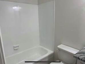 Bathroom features a bathtub and toilet, surrounded by white tile walls.