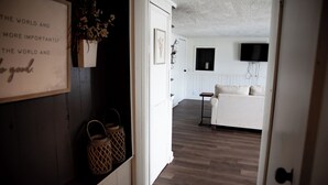 Ein Flur, der in ein Wohnzimmer mit einer Couch, einem an der Wand montierten Fernseher und einem gerahmten Zitat führt.