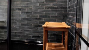Ein modernes Badezimmer mit Hocker aus Holz, dunkel gefliesten Wänden und einer Duschkabine aus Glas.