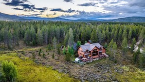 A large log cabin with a deck, surrounded by dense forest and mountains in the background. - Family-friendly cabin near Winter Park w/ hot tub (Fraser)