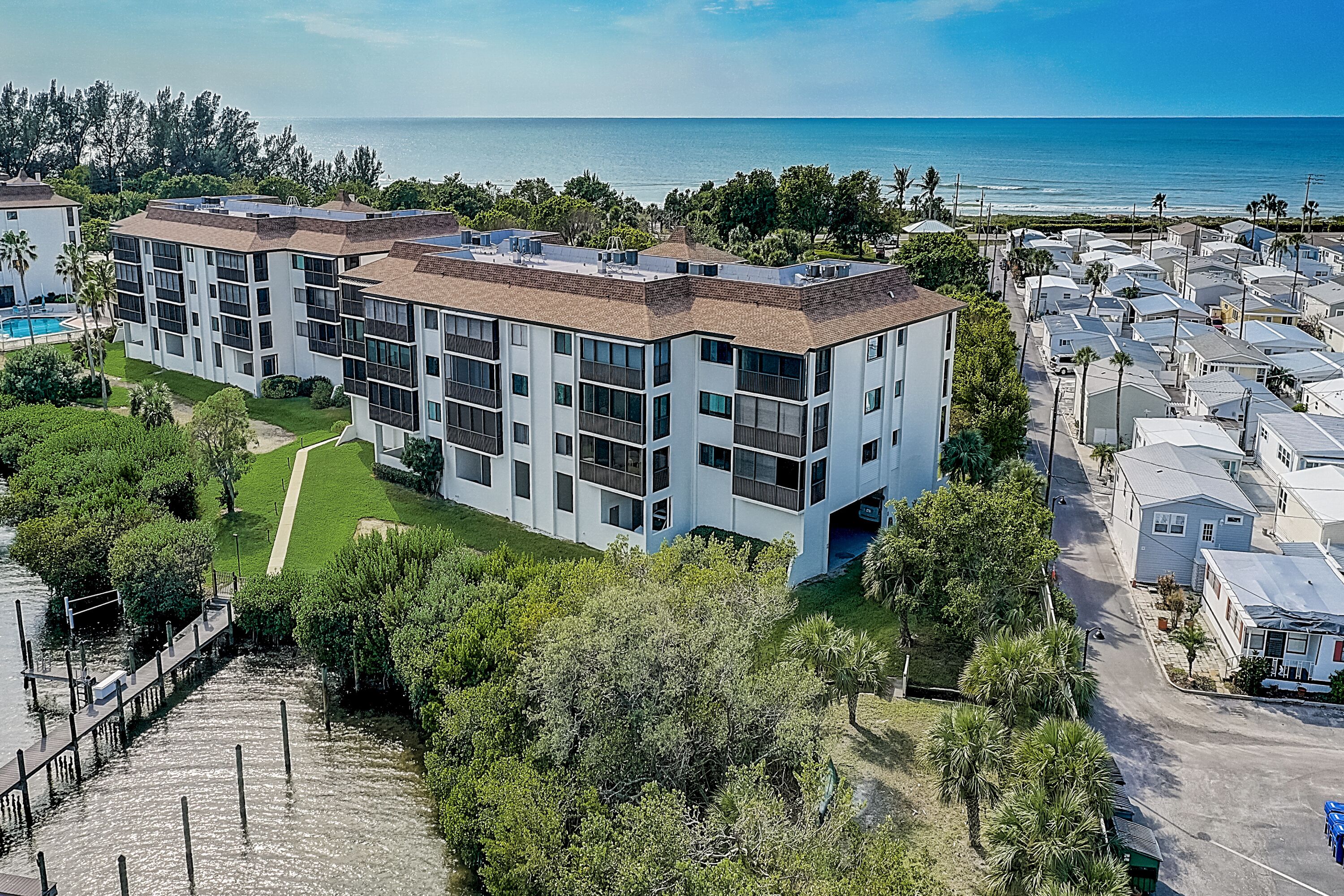 A modern multi-story building with a rooftop pool, surrounded by lush greenery and a view of the ocean.