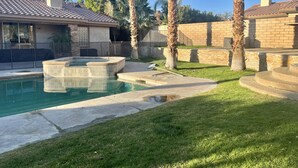 A backyard with a swimming pool, palm trees, and a brick house. - Rancho Mirage Home With Large Pool (Rancho Mirage)