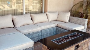 A sectional sofa with cushions, a stone fireplace, and a wicker coffee table. - Rancho Mirage Home With Large Pool (Rancho Mirage)