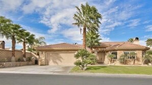 A two-story house with a tiled roof, a garage, and a well-maintained lawn with palm trees. - Rancho Mirage Home With Large Pool (Rancho Mirage)