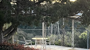Pátio externo com mesa e cadeiras, cercado por uma grade e vegetaç ão densa.
