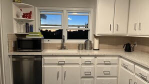 Cozinha moderna com armários brancos, lava-louças de aço inoxidável, micro-ondas e janela com vista para a cidade.