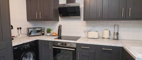 A compact kitchen with dark cabinets, a microwave, a toaster, a washing machine, and a sink.