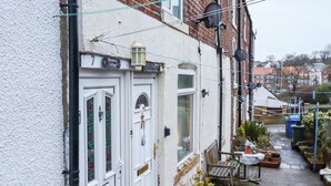 Ein schmaler Gang mit einer Reihe terrassenhausartiger Häuser, jedes mit einem einzigartigen Tür- und Fensterdesign. An der Seite des Ganges befinden sich Blumentöpfe und eine Bank.