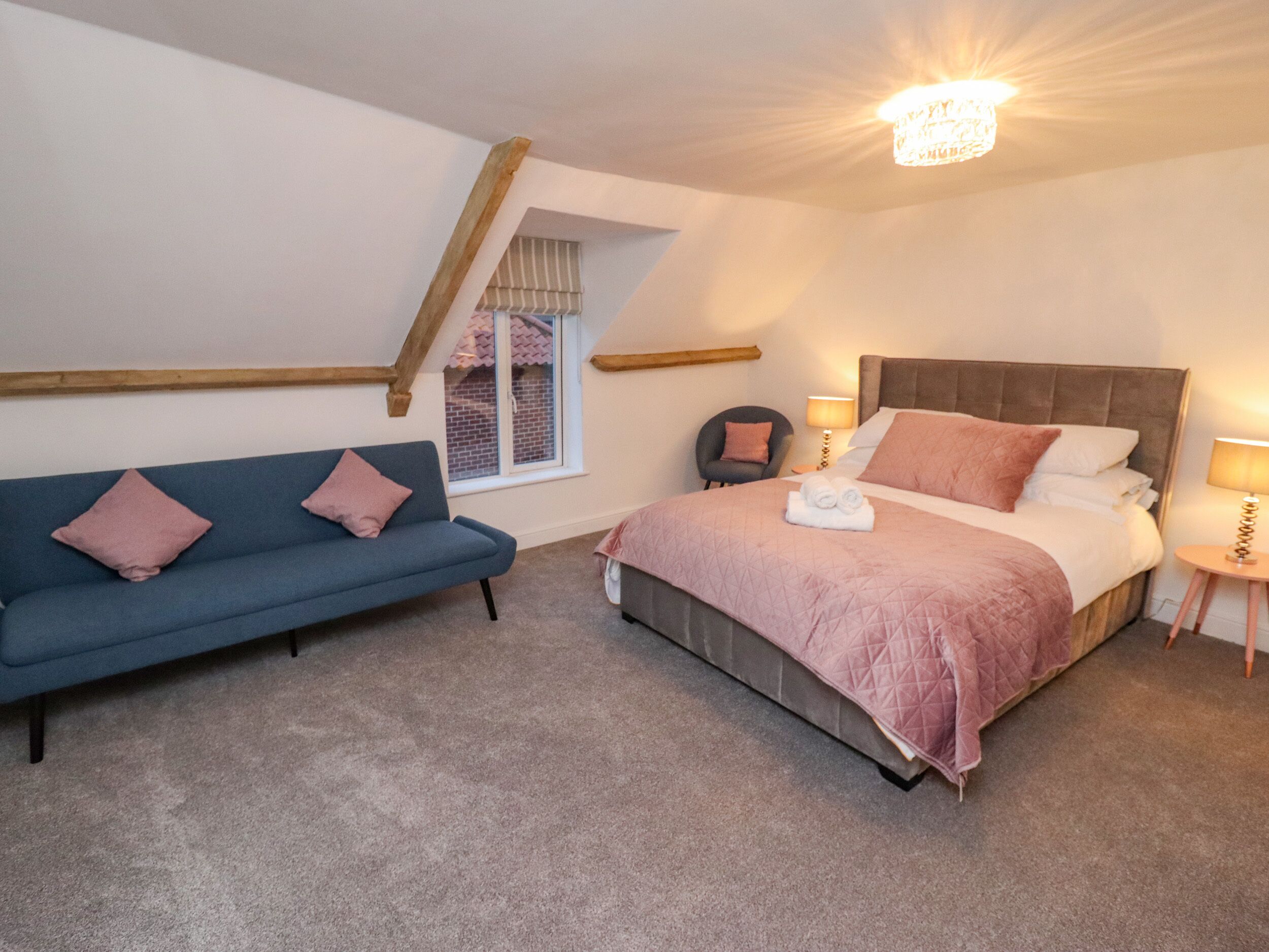 A bedroom with a bed, a blue sofa, a chair, a window, and a chandelier.