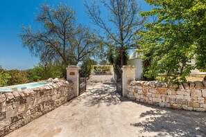 A stone pathway leading to a pool area with a view of trees and a building in the background.