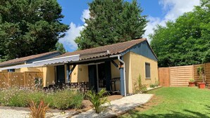 A single-story house with a patio, surrounded by a wooden fence and a garden with various plants and flowers. - Gîte in the heart of the Périgord Noir in a green, peaceful setting  (Saint-Crépin-et-Carlucet)